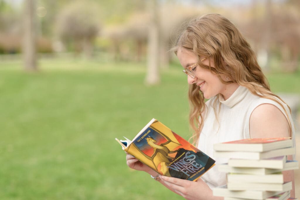 A graduating high school girl reads a novel during her colorful garden senior session with Salt Lake City photographer Jodi Cornwall Photography.