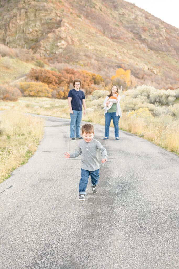 Little boy runs from family on fall trail