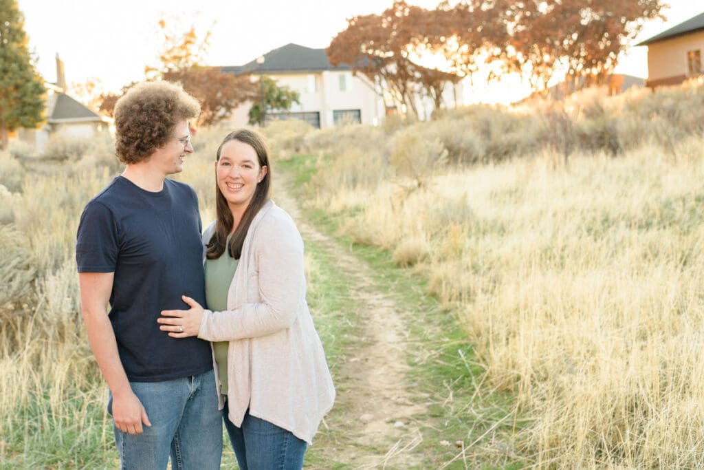 Husband and wife smiling together in a field who found a reason to schedule a couples session with Jodi Cornwall Photography.