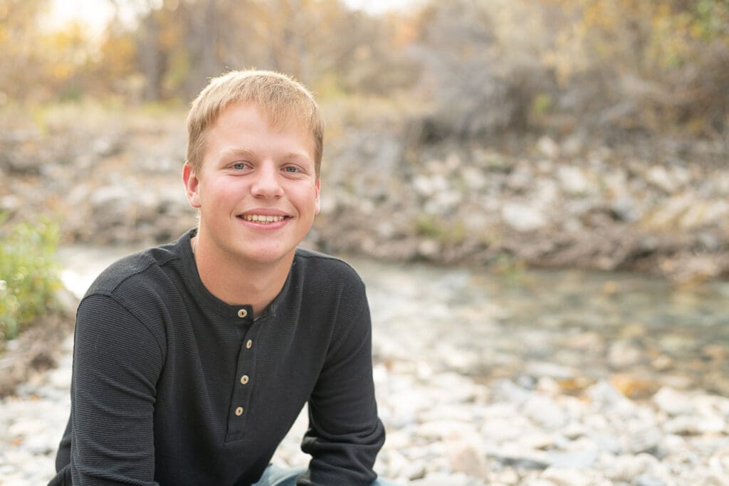 High school senior boy smiling by a river in the fall