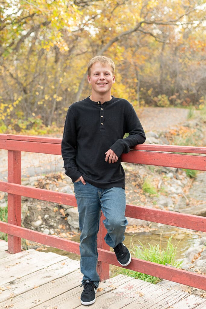 High school senior boy standing by a stream in the fall smiling.