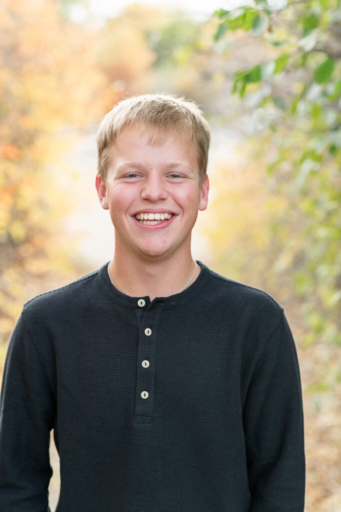 High school senior boy smiles in the fall leaves