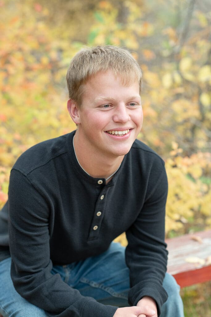 High school senior boy smiling with fall leaves in the background