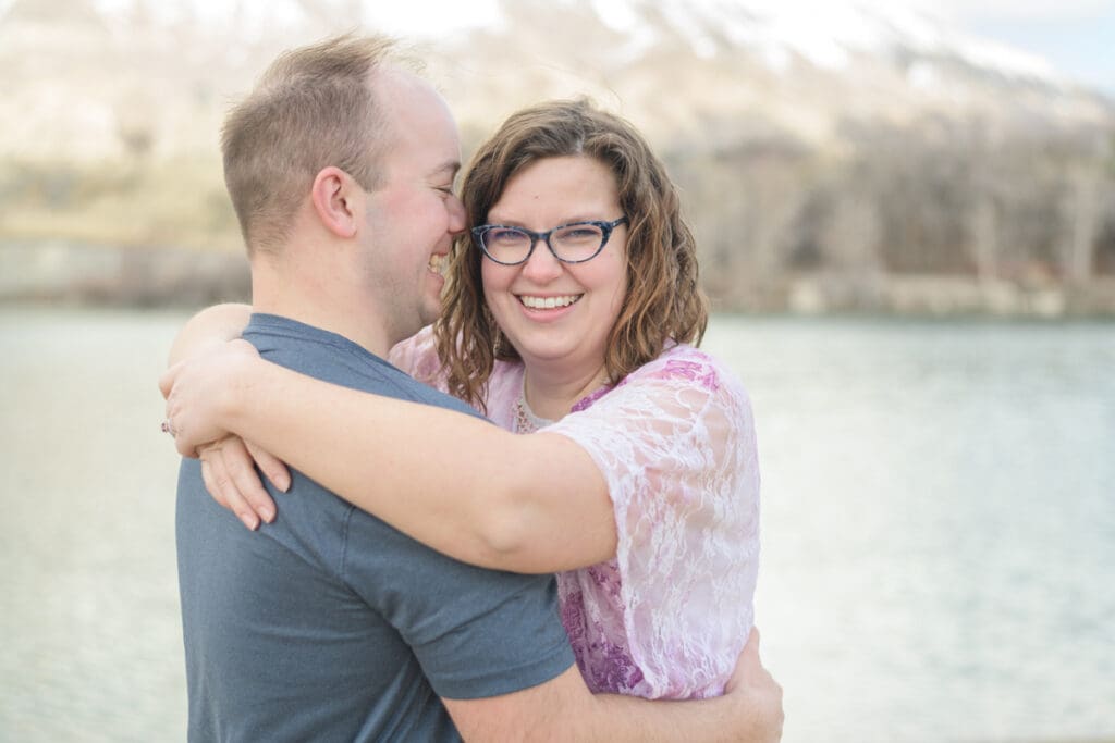An engaged couple hugs and the bride to be smiles at the camera during their joyful spring engagement session with Salt Lake photographer Jodi Cornwall Photography.