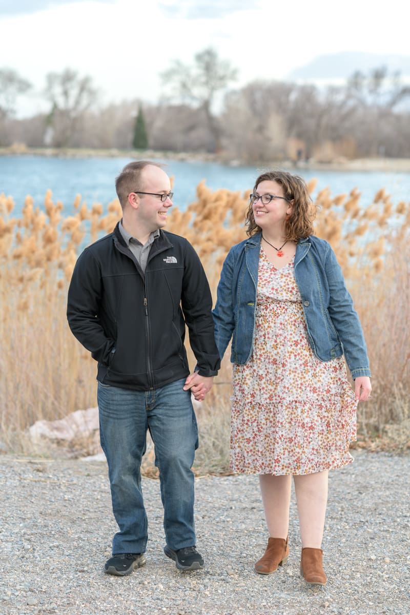 An engaged couple walks next to a pond during their joyful spring engagement session with Salt Lake photographer Jodi Cornwall Photography.