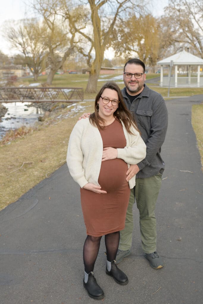 A husband stands with his pregnant wife smiling during their Murray Park maternity session.