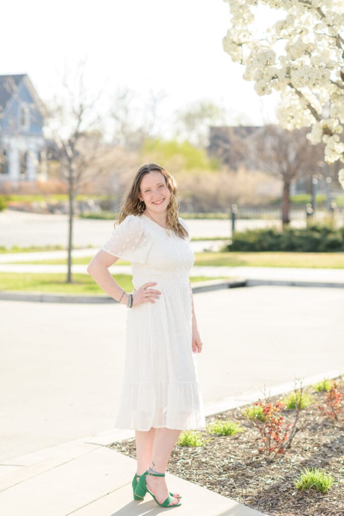 A woman smiles next to a flowering tree during her joyful spring downtown senior session with Jodi Cornwall Photography