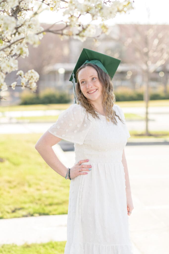 A woman smiles as she stands by a tree in bloom during her joyful spring downtown senior session with Jodi Cornwall Photography