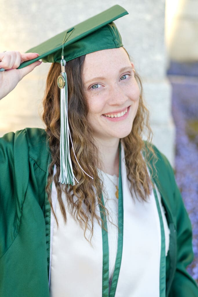 A woman smiles wearing her cap and gown during her joyful spring downtown senior session with Jodi Cornwall Photography