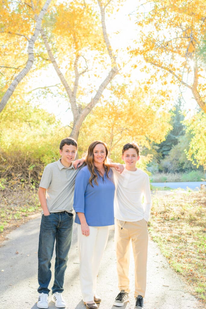 A mom and her teenage boys smile during a family photo session with fall colors