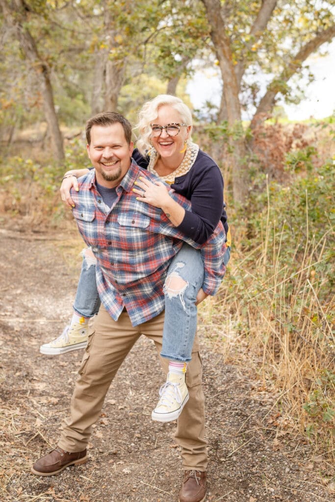Parents giving each other piggyback rides and laughing during a photo session.