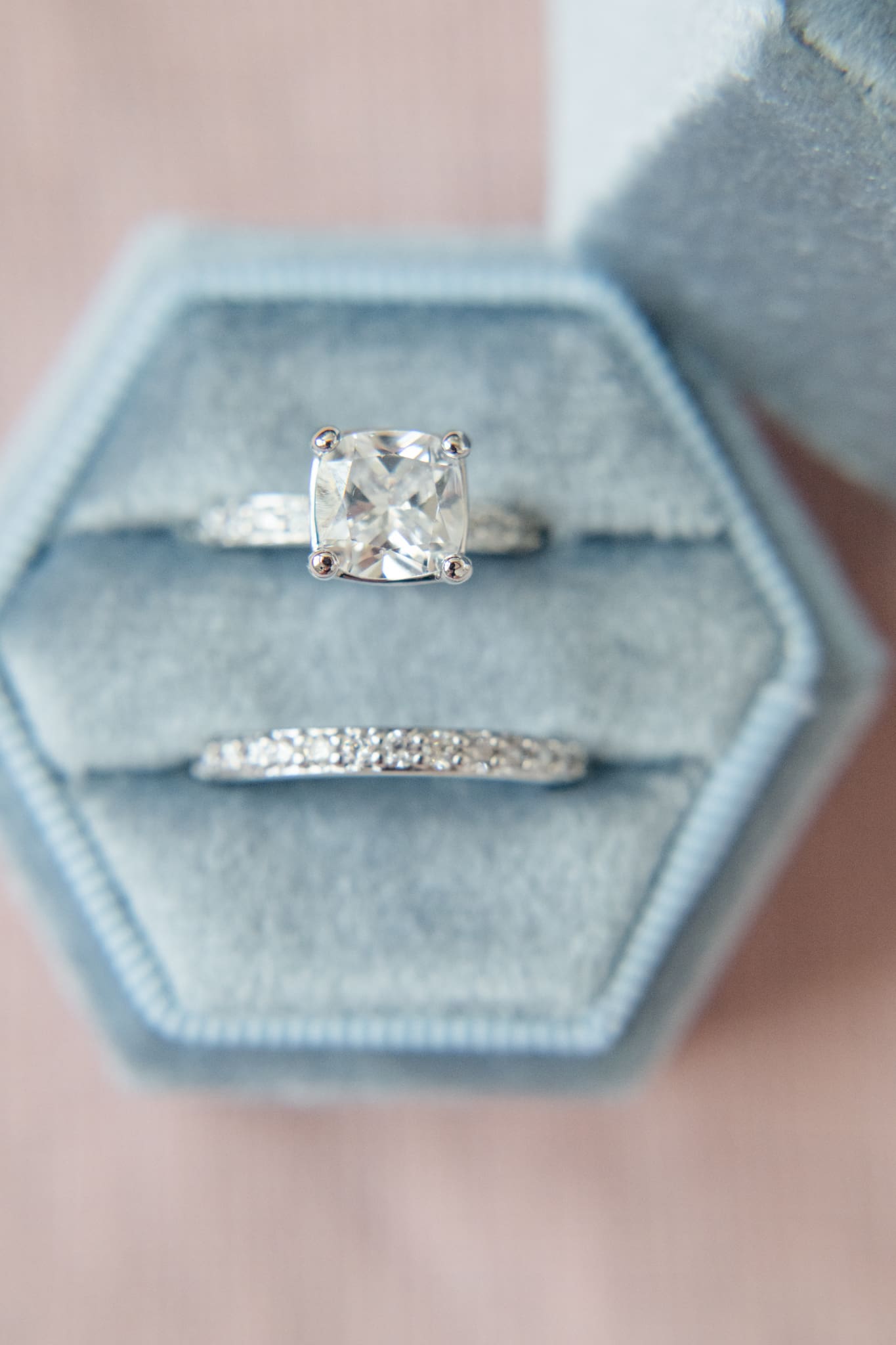 Detail image of an engagement ring set nestled in a dusty blue ring box on a rose colored backdrop.
