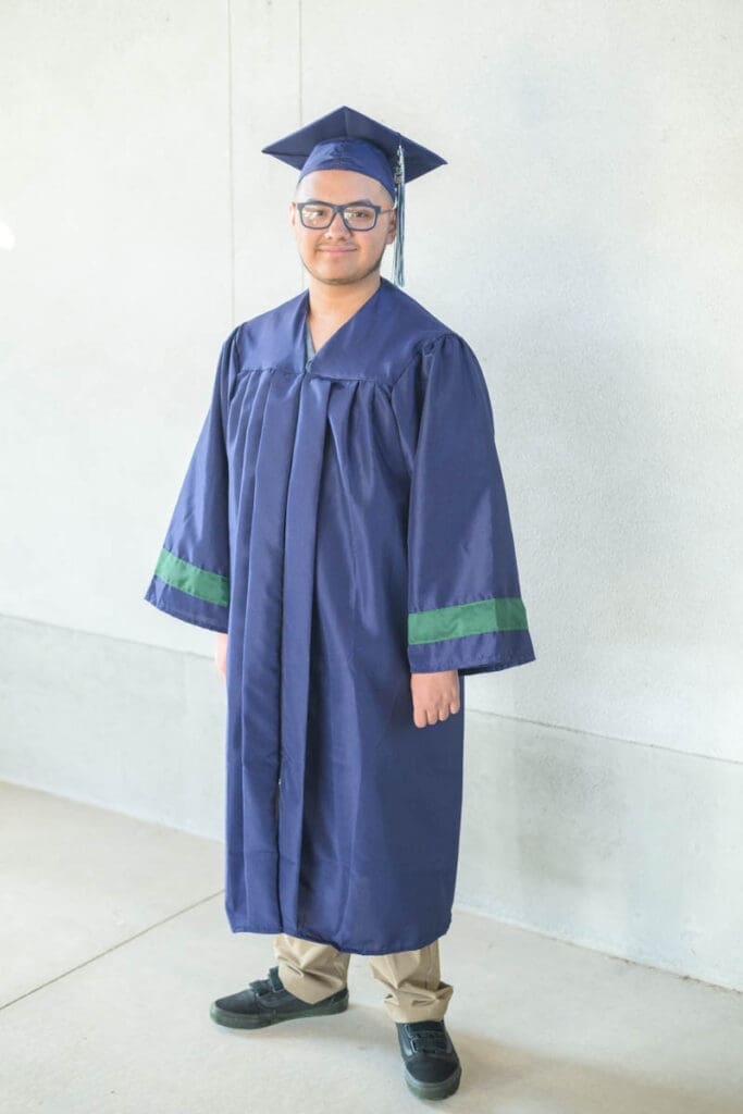A high school boy stands in his cap and gown during his conservation garden senior photos.