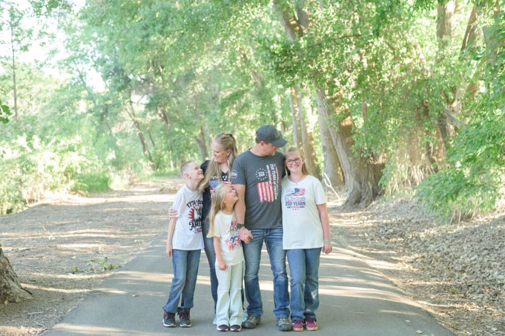 A family of five stands on a path and smiles at each other during family photos in Utah County.