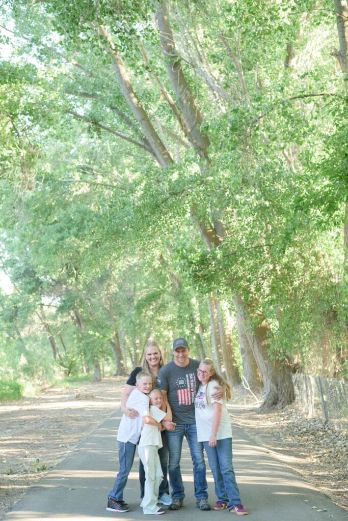 A family of five stands on a path and smiles at each other during family photos in Utah County.